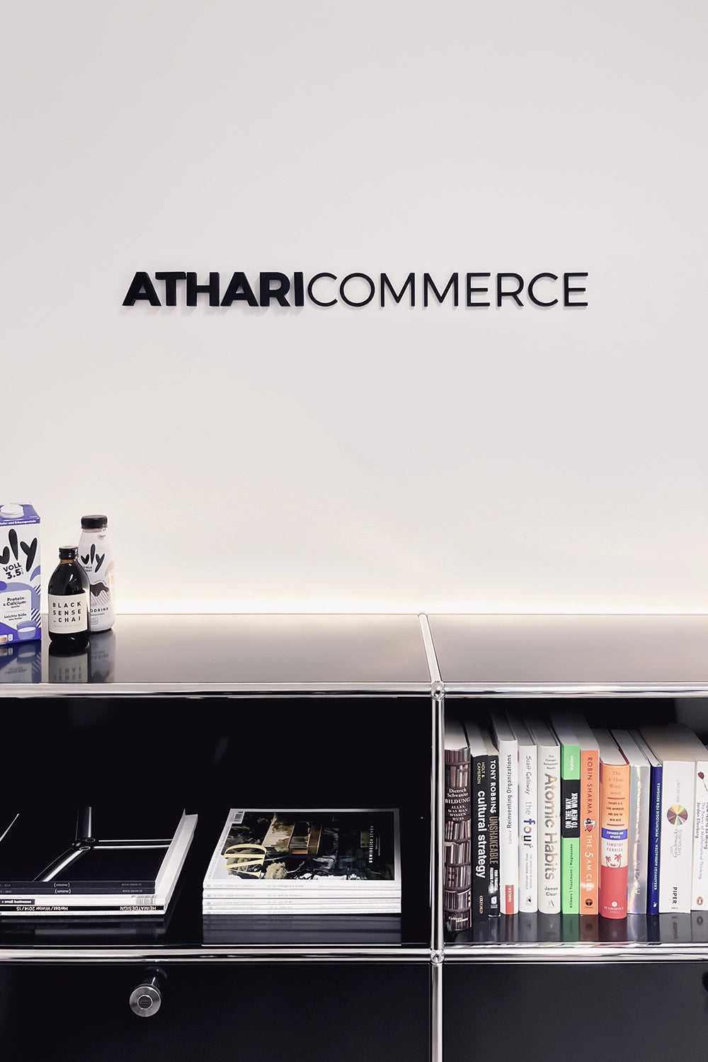 Schwarzes Regal mit Büchern und Getränken, darüber Text: ATHARICOMMERCE.