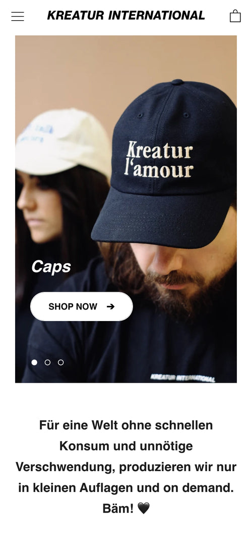 Zwei Personen mit Baseballkappen. Text auf Kappe: Kreatur l'amour.