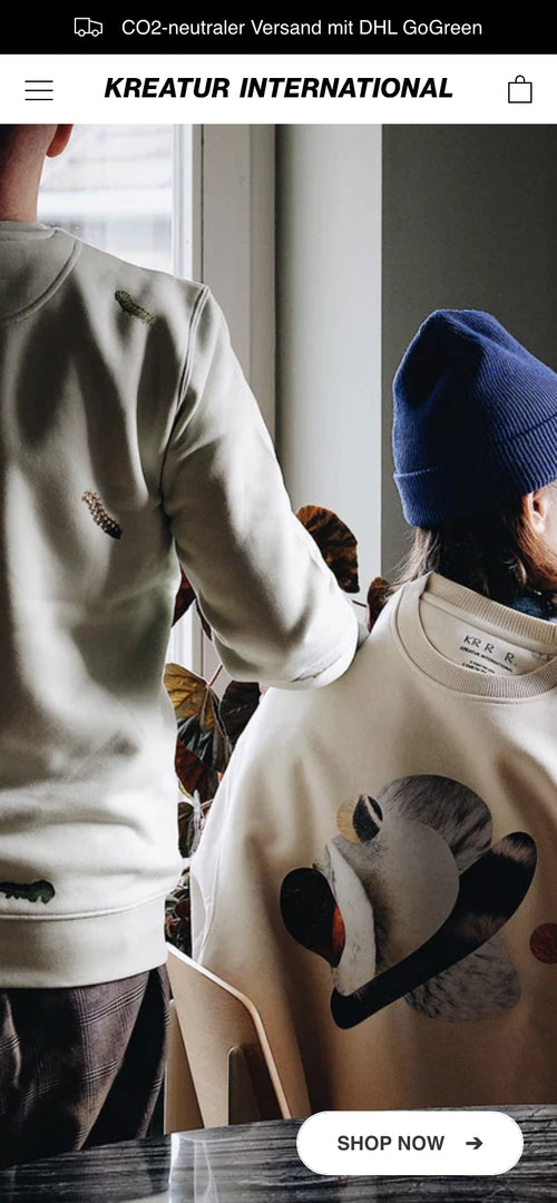 Zwei Personen in bedruckten Pullis sitzen am Tisch mit Pflanzen im Hintergrund.