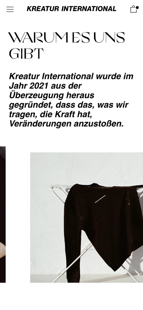 Schwarzes Kleidungsstück auf weißem Kleiderständer. Text über Gründung von Kreatur International.