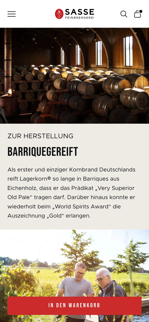 Männer in Brennerei, umgeben von Holzfässern; unterhalten sich.