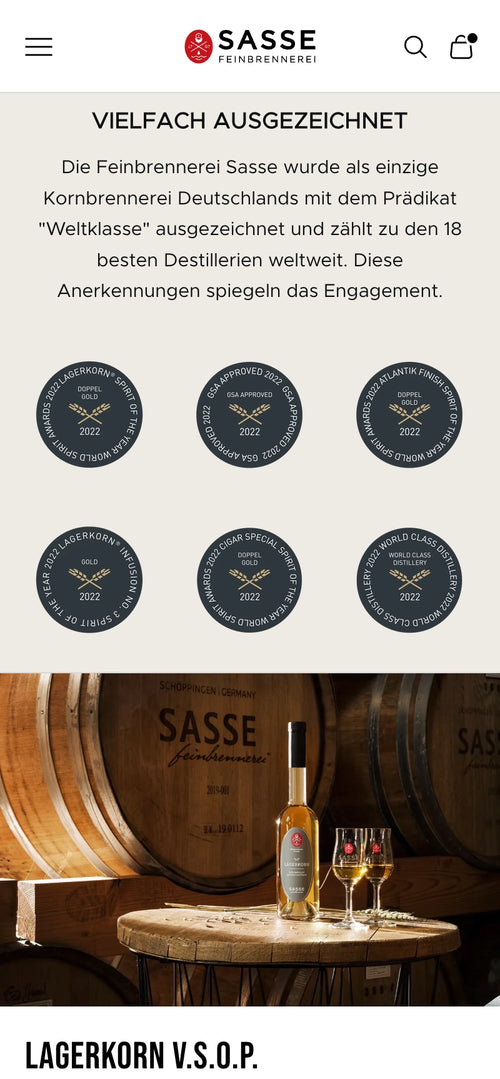Text über Auszeichnungen der Feinbrennerei Sasse. Flasche und Gläser vor Holzfässern.