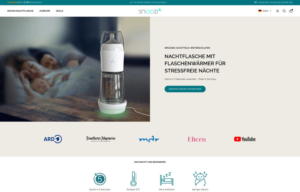 Schlafende Babys im Hintergrund, im Vordergrund steht eine beleuchtete Nachtflasche auf einem Tisch.