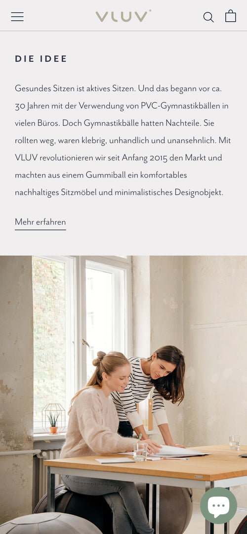 Zwei Frauen sitzen an einem Holztisch vor großen Fenstern und arbeiten an Dokumenten.