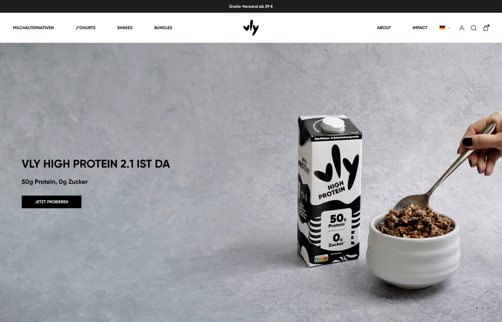 Eine Hand rührt Müsli, daneben steht eine Packung mit der Aufschrift 'Vly High Protein 2.1'.